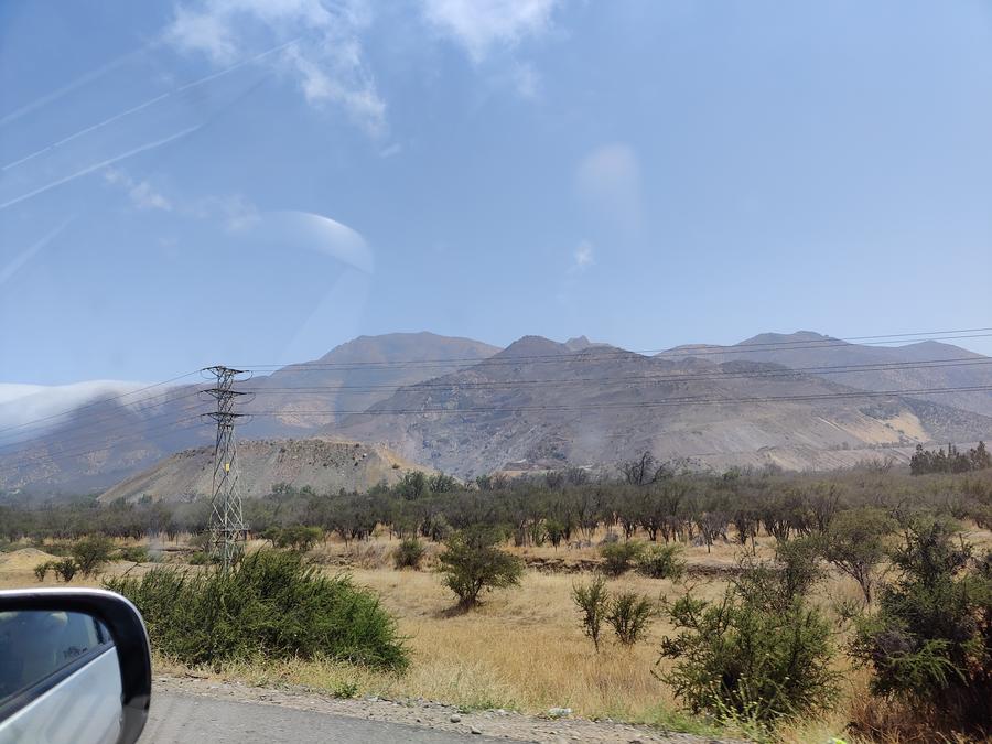 Photograph taken from a car of hills behind a low forest.