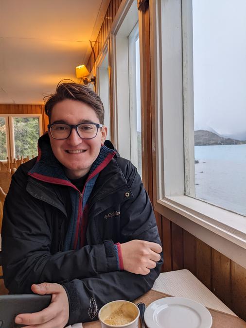 Nick sitting at a table with a coffee with a lake view.